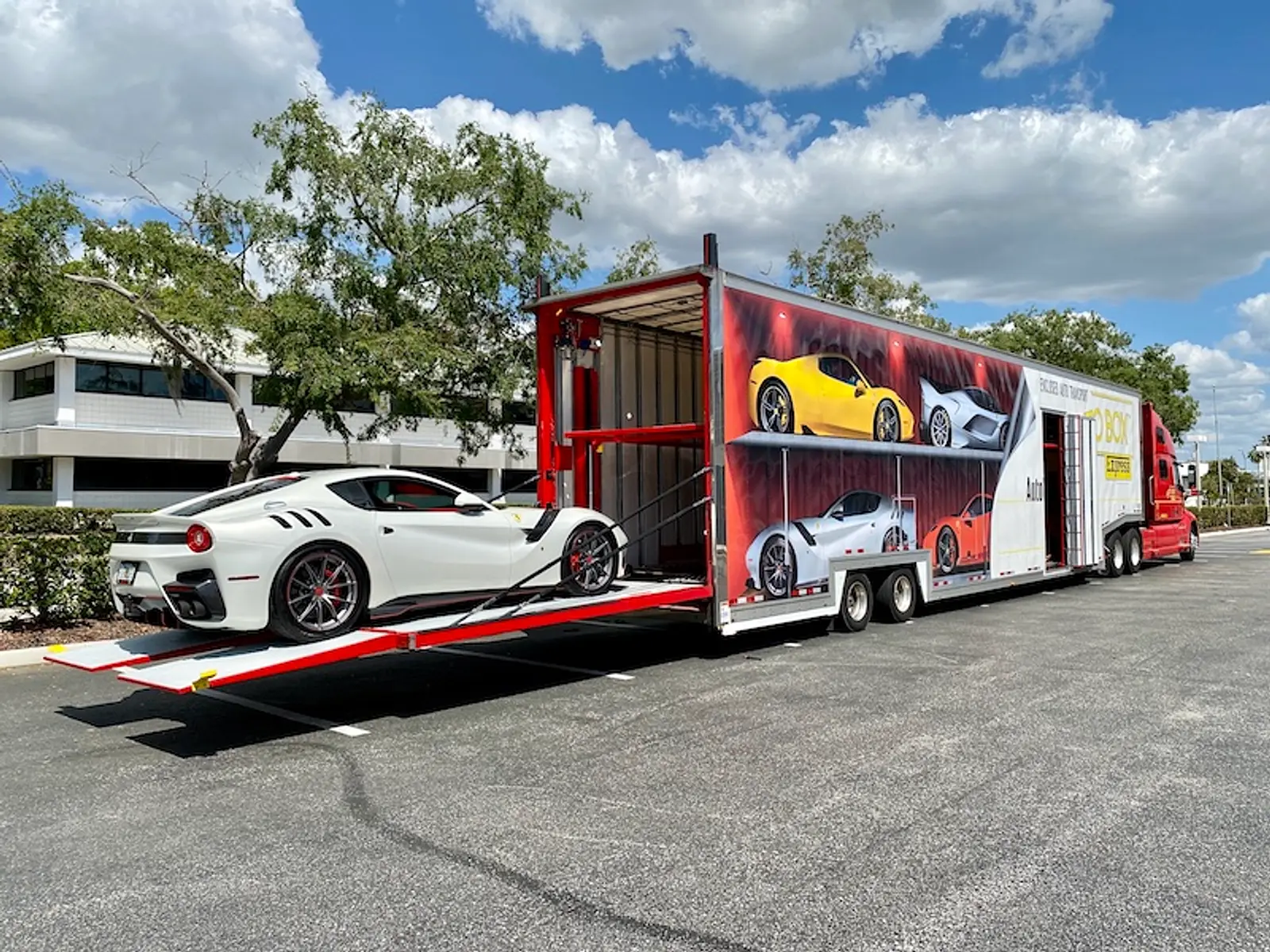 An AutoBox Express enclosed transporter with its ramps down and a white Ferrari being loaded